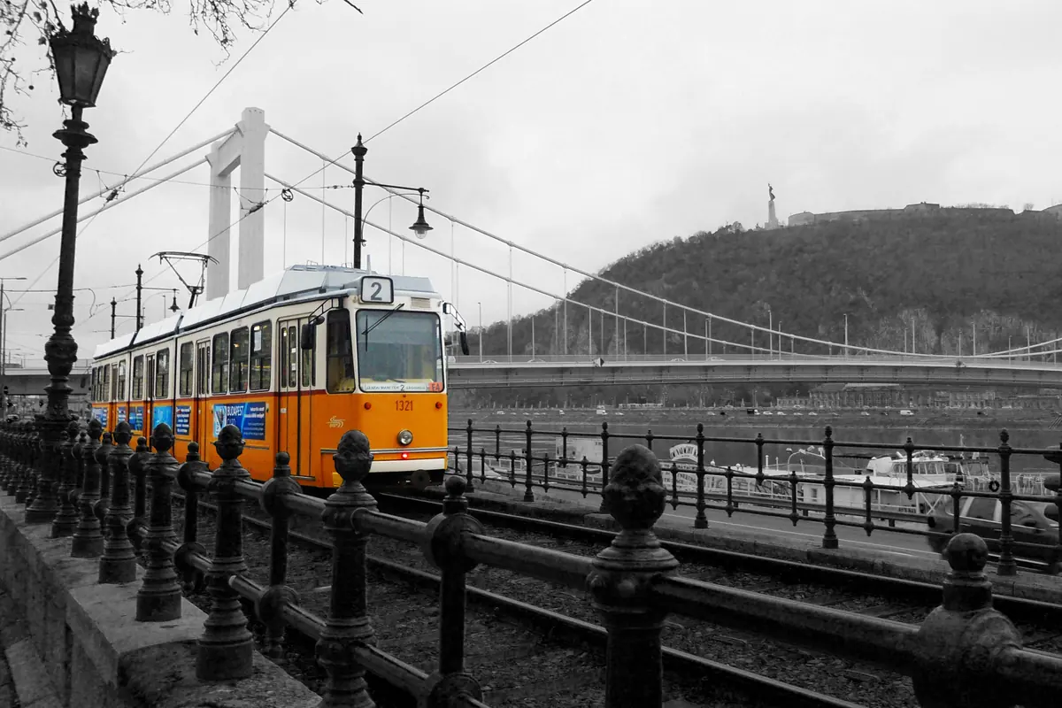 A yellow tram with the number 2 on the Pest embankment, with a Danube bridge and Gellért Hill behind it.